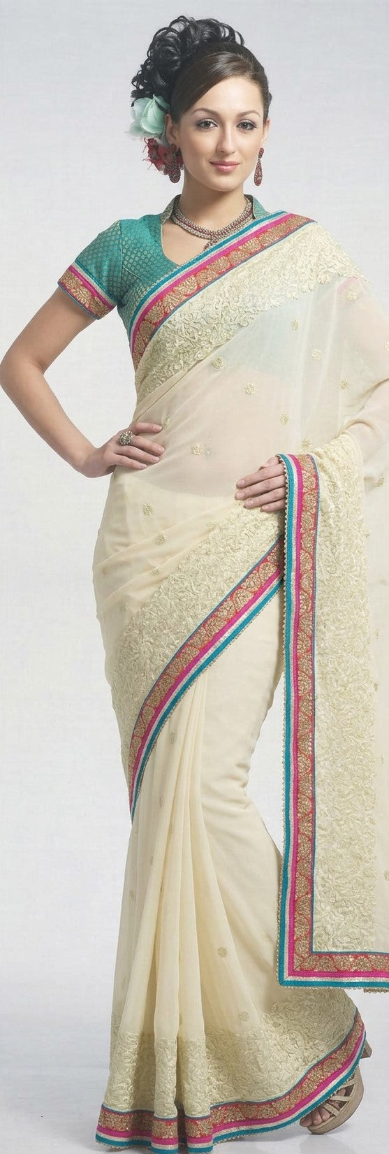 Ivory cream embroidered saree with teal-pink zari border and matching teal embroidered blouse, worn by a model against a plain background